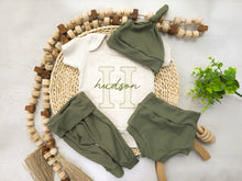 Load image into Gallery viewer, A personalized baby boy outfit with a white bodysuit featuring the text 'Hudson', accompanied by green baby pants and a hat, displayed on a wooden round tray with a decorative border.