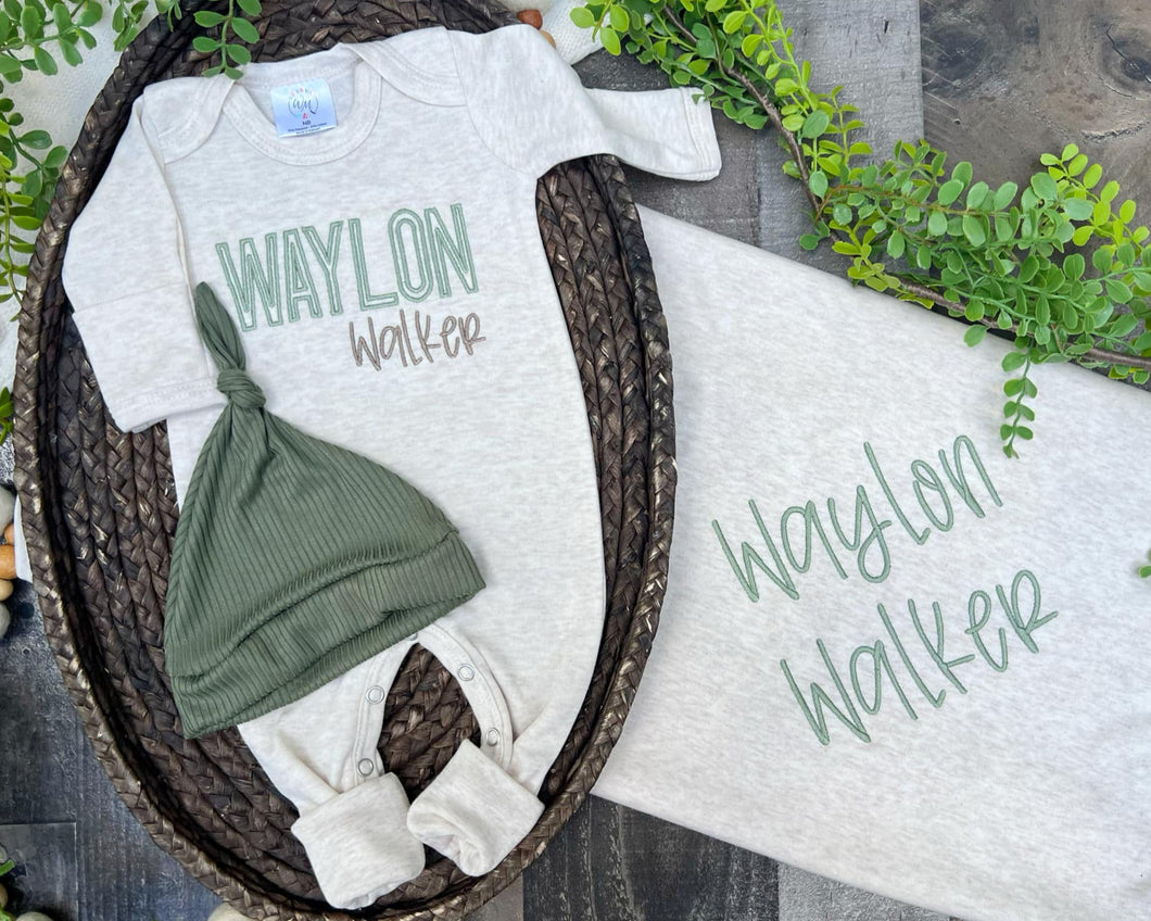 Baby outfit with onesie, hat, and blanket featuring 'Waylon Walker' on a wooden surface with greenery.