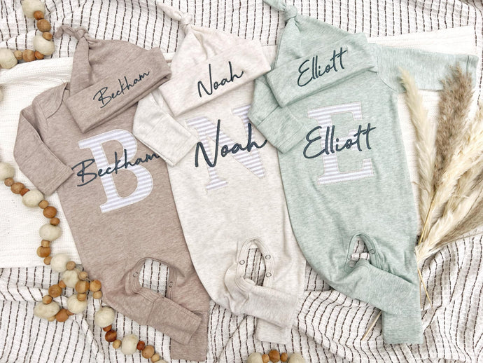 Three baby rompers with embroidered names on a textured surface.