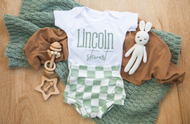 Baby outfit with onesie, pants, and toys on a wooden surface